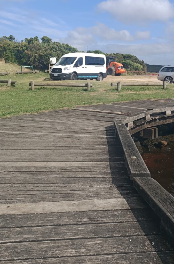 A picture of a boardwalk and a carpark with a sign for the next leg of the journey.