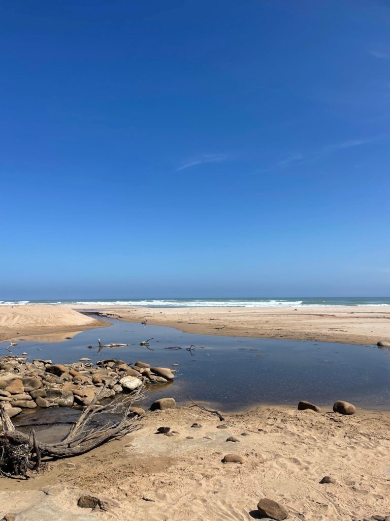 Beach with a river through the middle, blue skies with zero clouds.