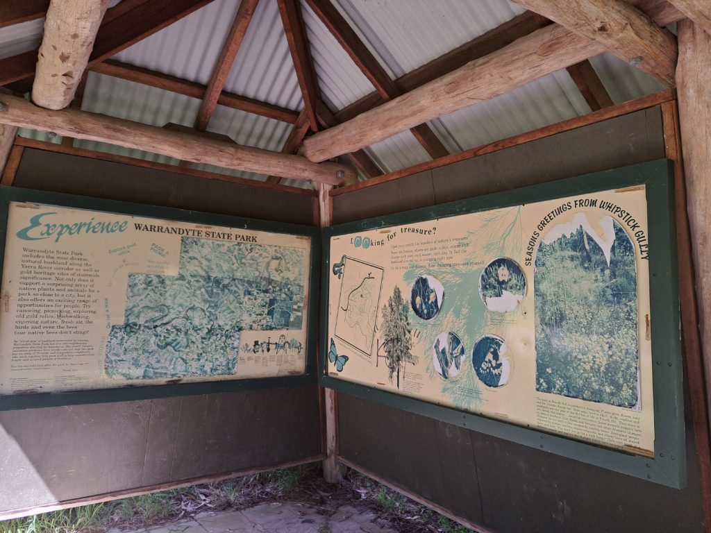 Picture underneath a shelter made of logs and corrugated iron sheets. On the walls of the shelter are informative signs about the history of the area.